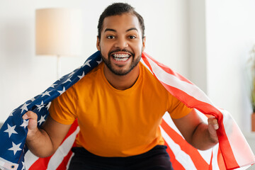 African American soccer fan with braces, shouting and celebrating a goal, holding a USA flag