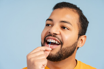 Cheerful African American man with braces, using an easy flosser on his teeth and looking away