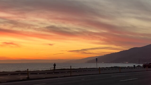 Anonymous, silhouetted person runs alongside the beach and Pacific Coast Highway at sunset, near Pacific Palisades, Los Angeles, California. Pacific Ocean and Santa Monica Mountains in background © vesperstock
