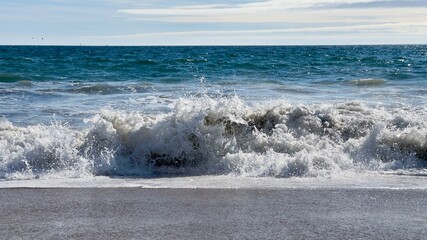 Fototapeta premium Close view of Pacific Ocean waves breaking on a sandy shore in Southern California on a bright, sunny day