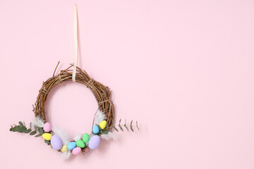 Beautiful wreath with Easter eggs and feathers on pink background