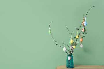 Branches decorated with Easter eggs in vase near color wall