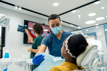 Female dental assistant preparing patient for a treatment while the male dentist is looking at...
