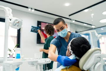 Female dental assistant preparing a patient for a dental surgery while the male oral surgeon is...