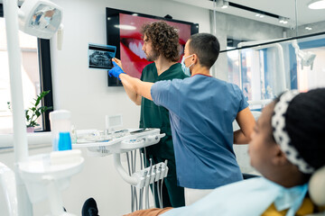 Two dental professionals discussing a x-ray image at a modern dental clinic while the patient is...