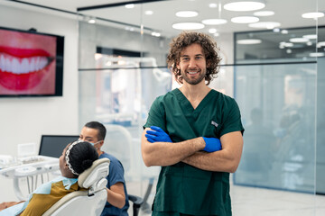 Portrait of a happy male professional dentist standing in his modern dental office, having his arms...