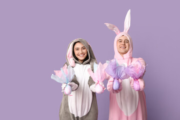 Beautiful young couple in bunny costume with Easter gift eggs on purple background