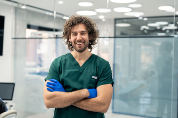Confident male professional dentist standing with crossed arms and smiling at camera while standing in his dental clinic.