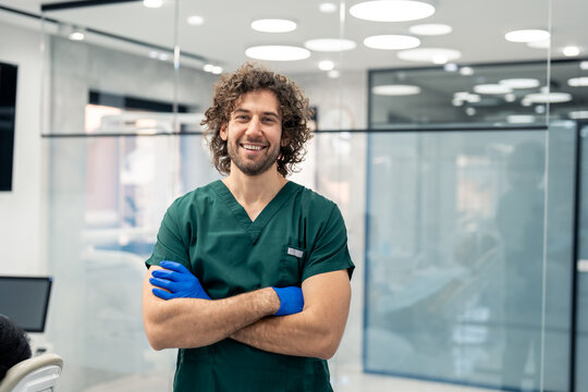 Proud young dental surgeon wearing green medical uniform posing for portrait photo in his clinic.