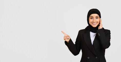 Smiling muslim businesswoman in hijab pointing to the side at free space