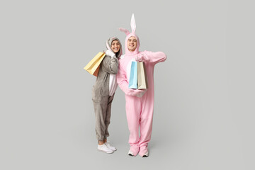 Beautiful young couple in bunny costume with shopping bags on grey background. Easter celebration