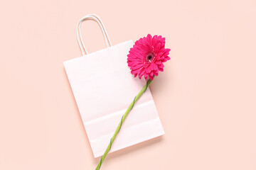 Paper shopping bag with gerbera flower on beige background