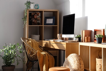 Modern workplace with computer, shelving unit and chair in light office