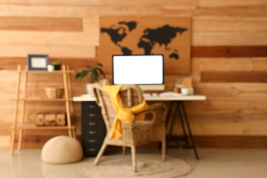 Beautiful workplace, computer and world map on wooden wall in stylish office, blurred view