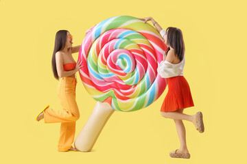 Female Asian friends with swim mattress on yellow background