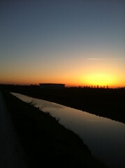 sunset with sun setting behind hill and canal with promenade