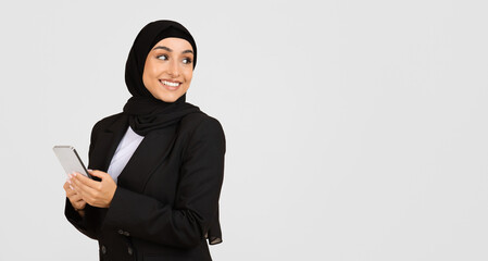 Muslim businesswoman in hijab smiling with smartphone, looking at free space