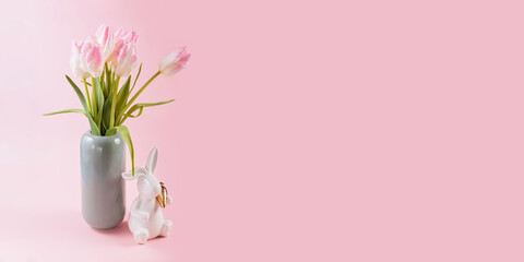 Pink tulips in vase and white Easter bunny figurine on pastel pink background