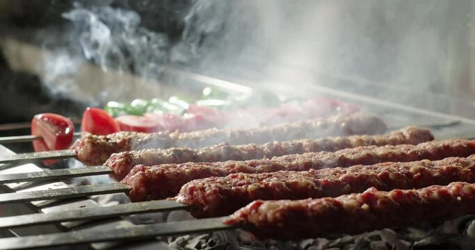 Close-up kebab barbecue on charcoal grill in a restaurant. Smoke rising over traditional Turkish kebab, tomatoes and peppers grilled on skewers