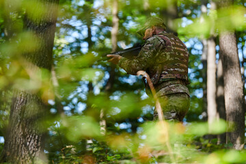 An elite soldier, camouflaged and stealthily navigating through dangerous woodland terrain, executes a covert mission in a secluded forest area