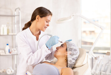 Professional female aesthetician administering hardware procedure on young woman using ion bubble...