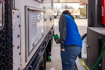 Man putting diesel fuel in truck with green handled pump at gas station.