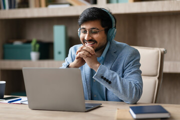 Fototapeta premium Hindu manager wearing earphones engaged in video call at workplace