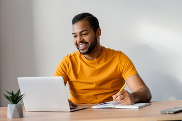 Smiling african american man with dental braces on teeth using laptop computer studying