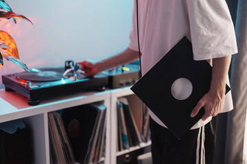 A person holding a vinyl record sleeve while using a turntable, with LPs in the background.