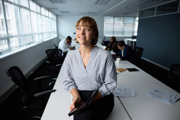 Happy young businesswoman in businesswear sitting on desk with digital tablet in office - 756810142