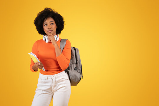 Pensive African American lady student with headphones and a gray backpack looks away