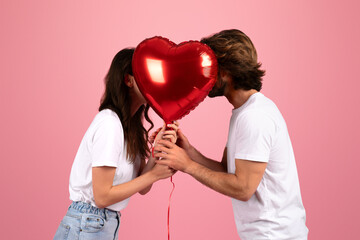 A loving couple in casual white t-shirts hidden behind a large red heart-shaped balloon