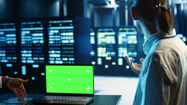 Engineering coworkers using mockup laptop to implement artificial intelligence parallel processing. Adept colleagues work on green screen device, enabling AI systems to process machine learning data