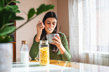 A young woman eating corn flakes for breakfast in the morning in her apartment	