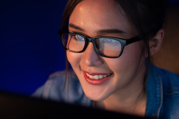 Portrait young beautiful Asian creative with glasses of smiling face looking on pc to search project creator social media online, planning strategy creator at neon modern office at night. Stratagem.