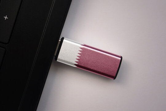 usb flash drive in notebook computer with the national flag of qatar on gray background.