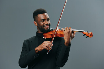 Elegant African American man in black suit playing violin against gray background for music and performance concepts