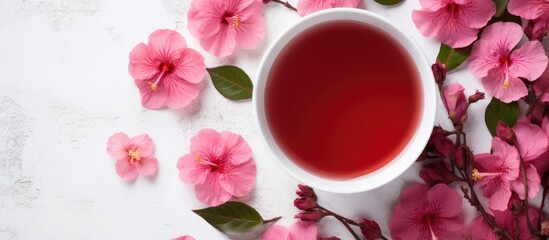 Obraz na płótnie Canvas A cup of red tea sits on a table adorned with pink flowers, creating a beautiful contrast between the liquid and the delicate petals