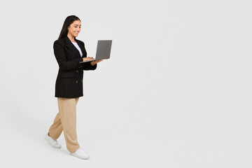 Smiling businesswoman walking with open laptop, free space