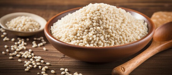 A bowl of rice, a staple food, sits next to a wooden spoon on a wooden table. Rice is a versatile ingredient used in various cuisines around the world