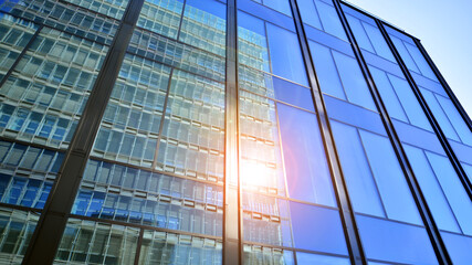 Obraz premium Modern office building with glass facade. Transparent glass wall of office building. Reflection of the blue sky on the facade of the building.