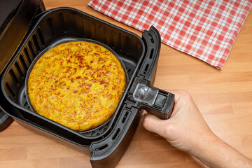 HAND COOKING POTATOES OMELETTE IN AIR FRYER AT THE KITCHEN. SPANISH FOOD RECIPES. TOP VIEW.