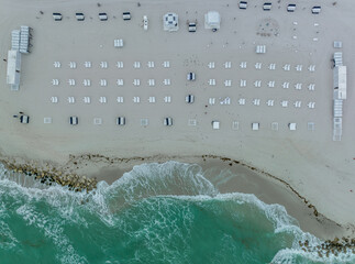 Aerial view of lounge beach chairs laid out in a patterns on Miami beach as the ocean waves crash