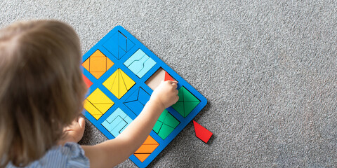 A cute girl is playing a logical wooden game on the floor in the room. Educational toy. 