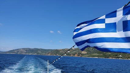 Podróż statkiem wzdłuż greckiego wybrzeża. Grecka flaga. Niebieskie niebo i wyspa 
