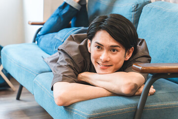 家のリビングでくつろぐ笑顔の若いアジア人・日本人男性（リラックス）
