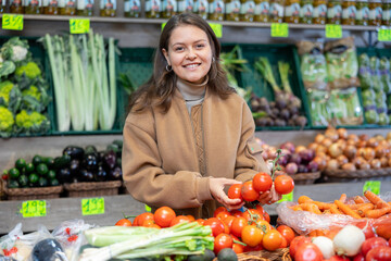Delighted young woman customer taking tomatoes from vegetable box in big greengrocery