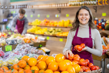 Female supermarket employee selling ripe tomatoes in the produce department