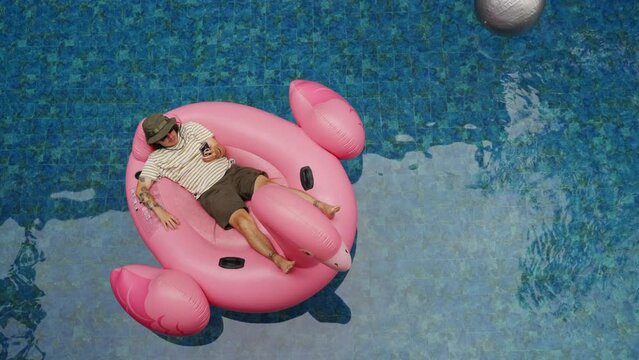 Aerial view of Man use phone on inflatable pink flamingo float mattress on pool party. 