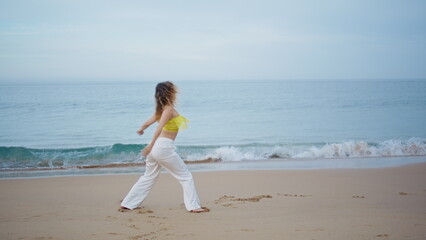 Fototapeta na wymiar Young lady dancing seashore in front picturesque ocean waves. Dancer performing